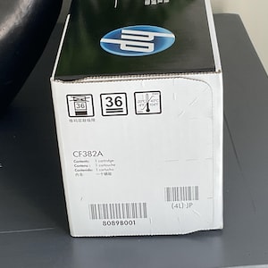 May include: A white and black HP printer cartridge box. The box has the model number CF382A and includes the text "Contents: 1 cartridge". The box also displays a barcode and the number "36".