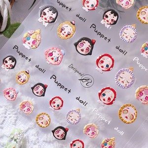 May include: A sheet of colourful nail art stickers featuring cartoon faces with different expressions. The stickers are designed to look like dolls with various hairstyles and clothing. The sheet is labelled "Puppet doll" and "Designed by AR".