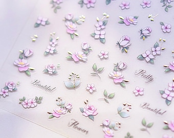 May include: A sheet of floral nail art stickers. The stickers feature various pink flowers, green leaves, and gold accents. The words "Beautiful", "Pretty", and "Flower" are printed on the sheet. The stickers are on a clear background.