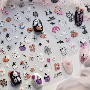 May include: Clear sheet of Halloween-themed nail art stickers. Designs include ghosts, pumpkins, spiders, bats, flowers, and cats. Some nails are painted with Halloween designs. The text "Happy Halloween" is visible.