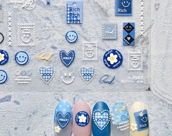 May include: Blue and white nail stickers with various designs, including hearts, smiley faces, flowers, and the words "Rich" and "Hello".
