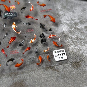 May include: Transparent sticker sheet with koi carp designs in orange, red, black, and white. The sheet also includes the text "Lucky Charm" and Chinese characters. A small white label with text is in the bottom right corner.