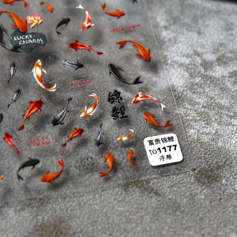May include: Transparent sticker sheet with koi carp designs in orange, red, black, and white. The sheet also includes the text "Lucky Charm" and Chinese characters. A small white label with text is in the bottom right corner.