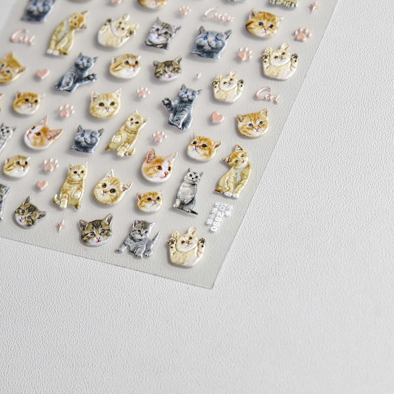 May include: A sheet of clear sticker paper with a variety of cute cat stickers. The stickers feature different colored cats with various expressions and poses. Some stickers have paw prints and hearts around them.