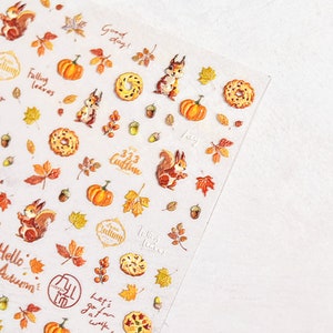 Puede incluir: Una hoja de pegatinas transparentes con tem&aacute;tica oto&ntilde;al. Las pegatinas representan ardillas, calabazas, hojas, bellotas y donuts. El texto en las pegatinas incluye "Good day!", "Falling leaves", "It's Autumn", "Hello Autumn", "333 Cudtine", "Hey", "Let's go for a walk", y "Falling leaves".