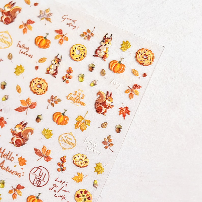Puede incluir: Una hoja de pegatinas transparentes con tem&aacute;tica oto&ntilde;al. Las pegatinas representan ardillas, calabazas, hojas, bellotas y donuts. El texto en las pegatinas incluye "Good day!", "Falling leaves", "It's Autumn", "Hello Autumn", "333 Cudtine", "Hey", "Let's go for a walk", y "Falling leaves".
