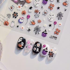 May include: A sheet of Halloween-themed nail art stickers featuring ghosts, pumpkins, flowers, spiders, and spiderwebs. Five painted fingernails showcase the sticker designs. The text "to 5205 万圣节一浮雕" is visible.
