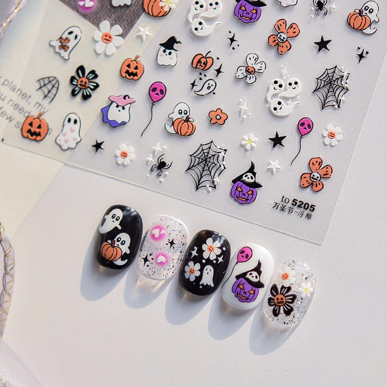 May include: A sheet of Halloween-themed nail art stickers featuring ghosts, pumpkins, flowers, spiders, and spiderwebs. Five painted fingernails showcase the sticker designs. The text "to 5205 万圣节一浮雕" is visible.