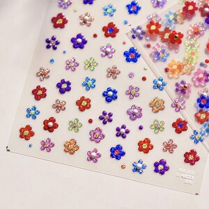 May include: A sheet of colorful flower stickers with glitter accents. The stickers are arranged in a grid pattern and feature a variety of colors, including red, blue, green, purple, and yellow.