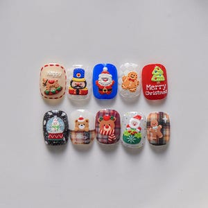 May include: Ten Christmas-themed nail art designs featuring various holiday characters and symbols, including a snowman, gingerbread man, Santa Claus, a nutcracker, and a Christmas tree. The designs are painted on white nail tips.