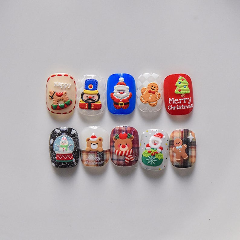 May include: Ten Christmas-themed nail art designs featuring various holiday characters and symbols, including a snowman, gingerbread man, Santa Claus, a nutcracker, and a Christmas tree. The designs are painted on white nail tips.