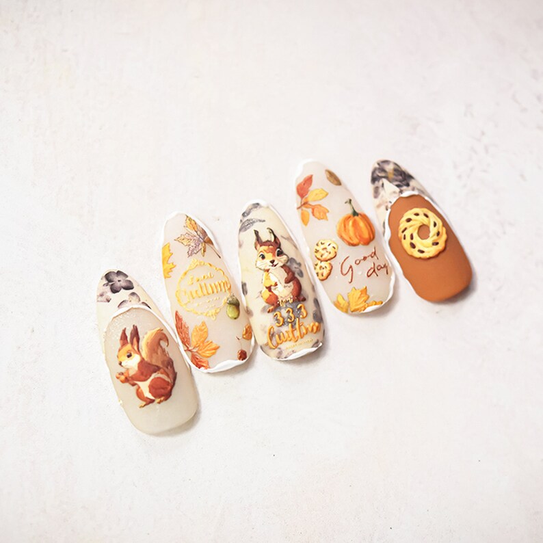 Puede incluir: Cinco dise&ntilde;os de u&ntilde;as con tem&aacute;tica oto&ntilde;al que incluyen una ardilla, hojas, calabazas y el texto "Good day" y "Fall Autumn".