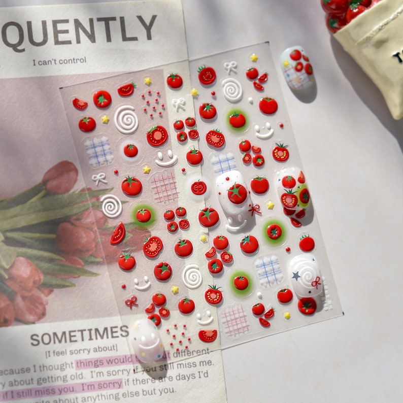 May include: Clear sheet of nail art stickers featuring red tomato designs, white swirls, and smiley faces. The sheet includes various sizes of tomatoes and decorative elements. The text "QUENTLY" and "SOMETIMES" are visible.