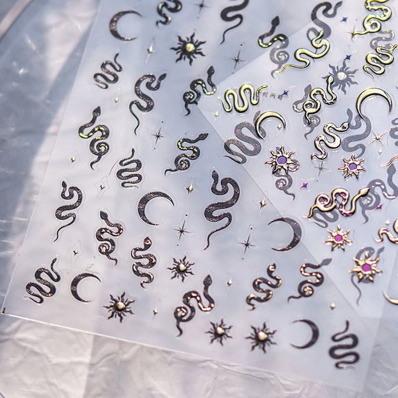 May include: A sheet of clear sticker paper with gold and black snake, crescent moon, and sun designs. The stickers are perfect for adding a touch of whimsy to journals, laptops, and other surfaces.