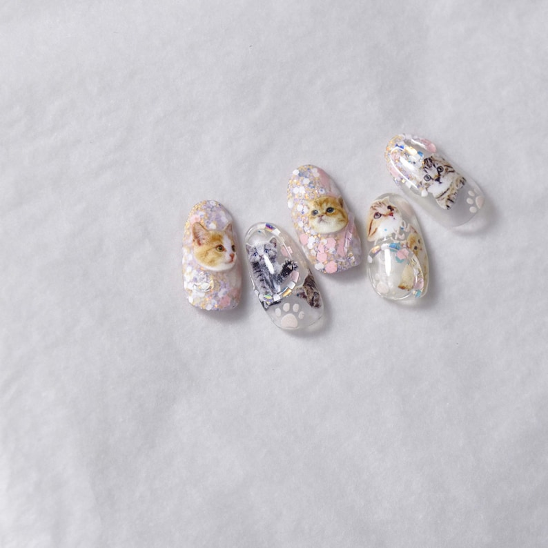 May include: Five clear nail polish colors with glitter and cat designs. The designs include a cat face, a cat paw print, and a cat tail.