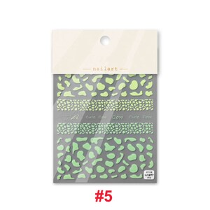 Op de afbeelding: Een pakje nagelkunst stickers met een koe print ontwerp. De stickers zijn groen en wit en hebben de tekst "cute cow" erop. Het pakje is gelabeld met het nummer "#5".