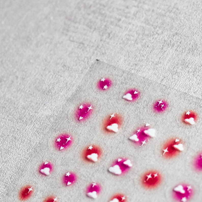 May include: A sheet of pink and white nail stickers with a cloud and star design.