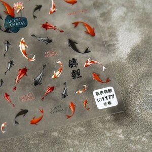 May include: Transparent sticker sheet with koi carp designs in red, orange, black, and white. Some stickers have the words "Lucky Charm". A small white label with Japanese text is in the corner.