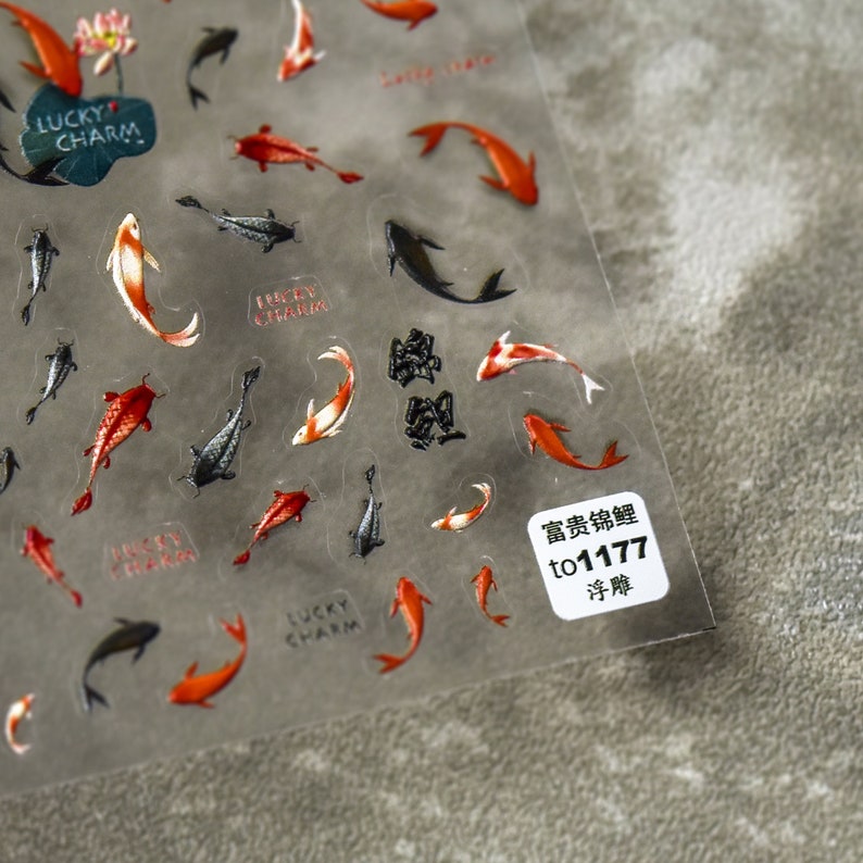 May include: Transparent sticker sheet with koi carp designs in red, orange, black, and white. Some stickers have the words "Lucky Charm". A small white label with Japanese text is in the corner.