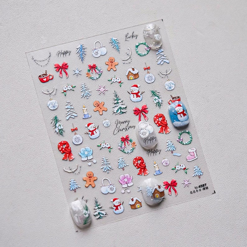 May include: A sheet of clear nail stickers with a variety of Christmas-themed designs, including snowmen, gingerbread men, presents, and wreaths. The stickers are arranged in rows and columns on a white background. The text "Happy Christmas" is featured on the sheet.