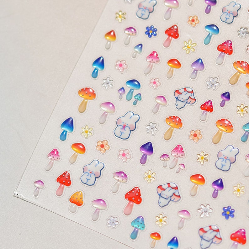May include: A sheet of colorful mushroom and flower stickers. The stickers are glossy and have a 3D effect. There are various colors of mushrooms, including red, orange, yellow, green, blue, and purple. The flowers are white and yellow.