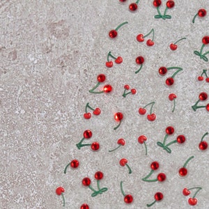 May include: A sheet of red and green cherry stickers on a light gray background. The cherries are arranged in a random pattern.
