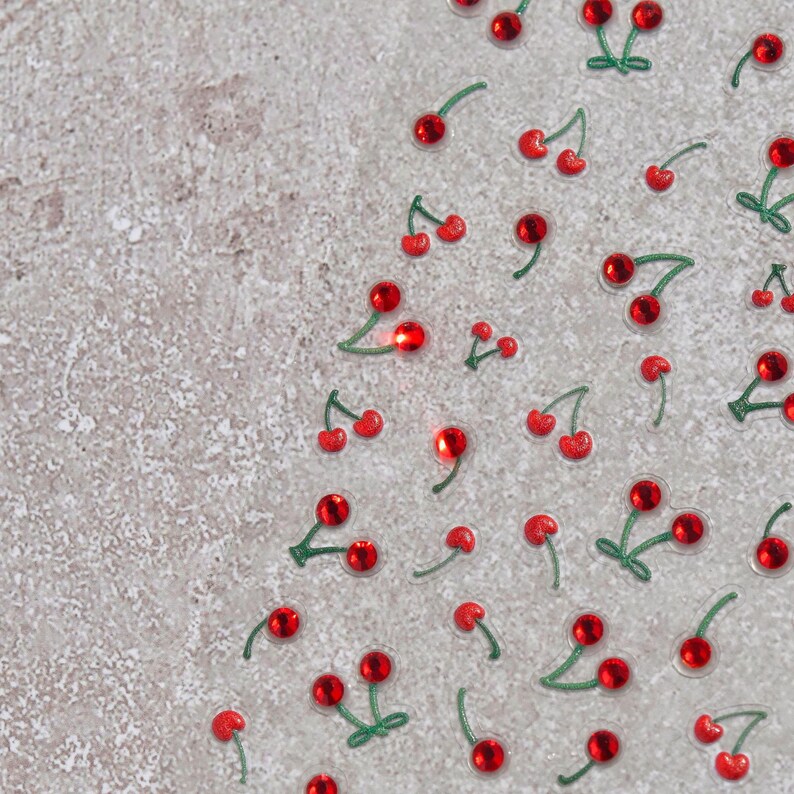 May include: A sheet of red and green cherry stickers on a light gray background. The cherries are arranged in a random pattern.