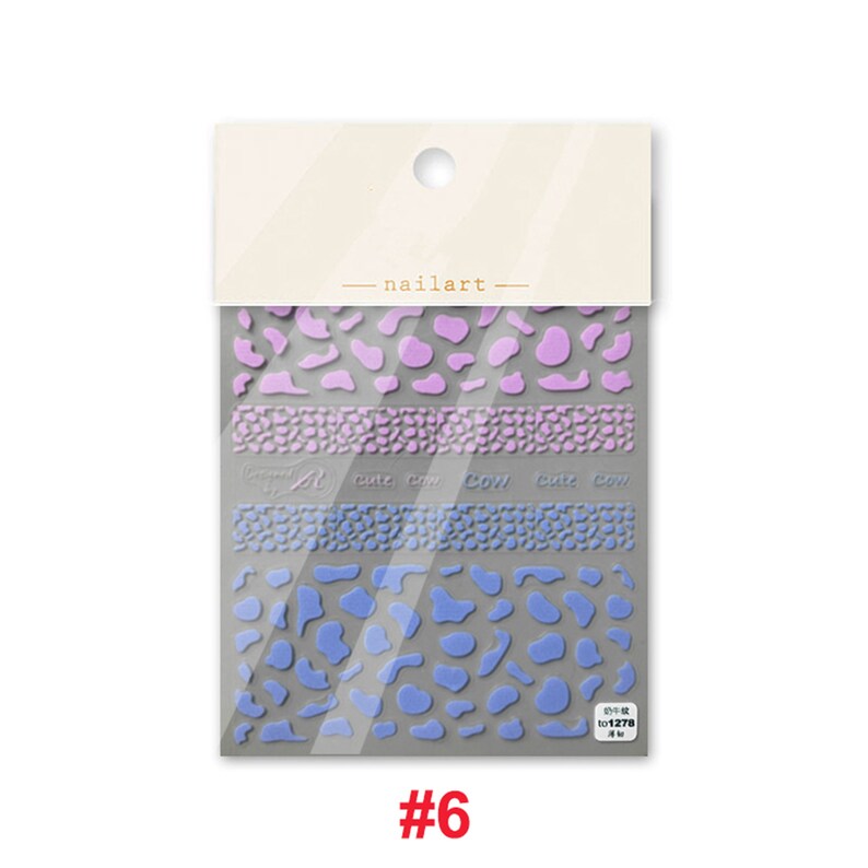 Op de afbeelding: Een pakje nagelkunst stickers met een koe-print ontwerp in tinten paars en blauw. De stickers zijn gelabeld "cute cow" en worden geleverd in een doorzichtige plastic zak met een wit label waarop "nailart" staat.
