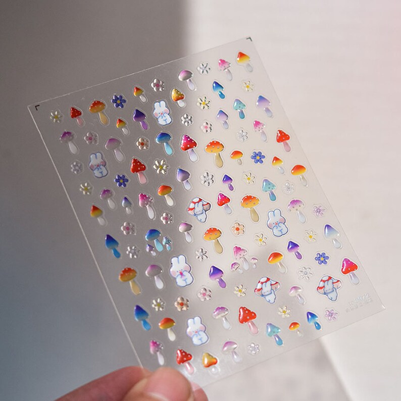 May include: A sheet of colorful, iridescent stickers featuring mushrooms, flowers, and bunnies. The stickers are perfect for adding a whimsical touch to journals, planners, and other craft projects.