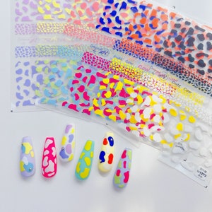 Op de afbeelding: Een set van acht koe-print nagel stickers in verschillende kleuren, waaronder roze, geel, blauw en groen. De stickers zijn in een rij op een wit oppervlak gerangschikt. De stickers zijn ontworpen om op vingernagels te worden aangebracht.