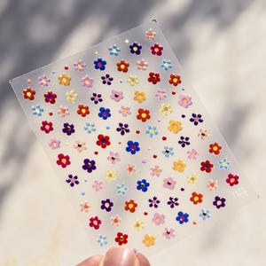 May include: A sheet of colorful flower stickers with gold accents. The stickers are arranged in a repeating pattern on a clear plastic sheet.