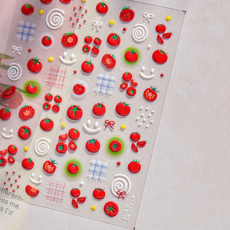 May include: Clear sticker sheet with a repeating pattern of red tomatoes, bows, stars, and white swirls. Some tomatoes are sliced, and others are whole. There are also small grid and smiley face designs.