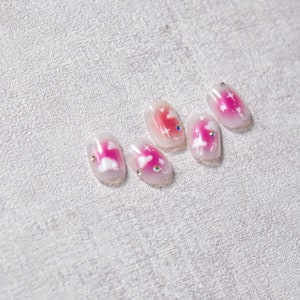 May include: Five pink and white fake nails with a cloud and star design. Each nail has a small clear rhinestone.