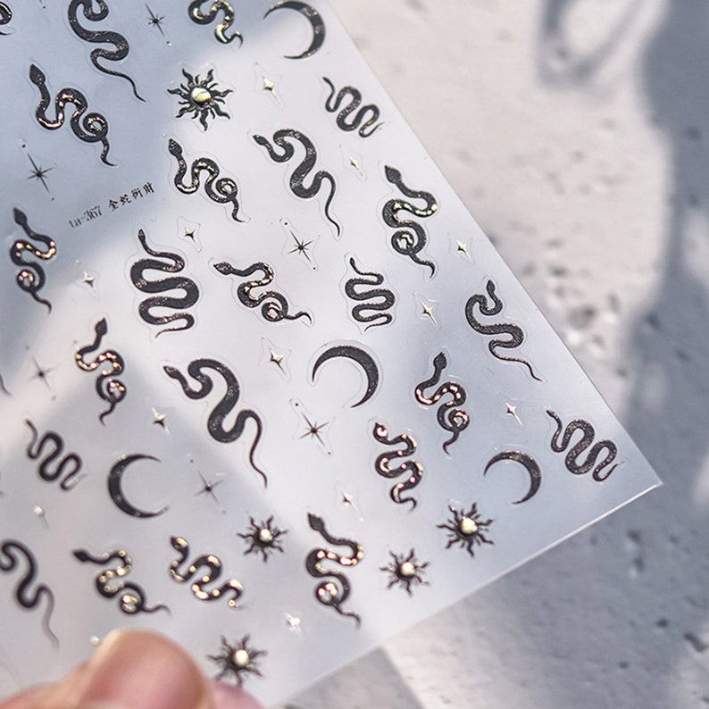 May include: A sheet of clear sticker paper with silver and black snake, moon, and star stickers. The text "Ln. 267" is printed on the sheet.