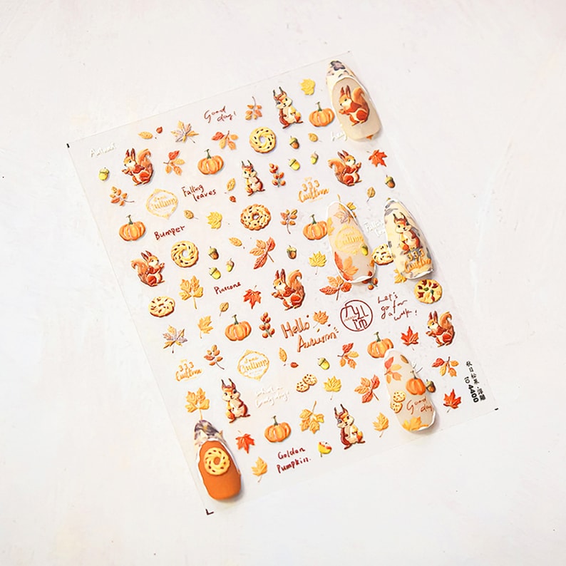 Puede incluir: Una hoja de pegatinas para u&ntilde;as con tem&aacute;tica oto&ntilde;al con ardillas, calabazas, hojas, bellotas y rosquillas. Las pegatinas tienen el texto "Good Day", "Falling Leaves", "Hello Autumn", "Golden Pumpkin" y "Let's go for a walk".