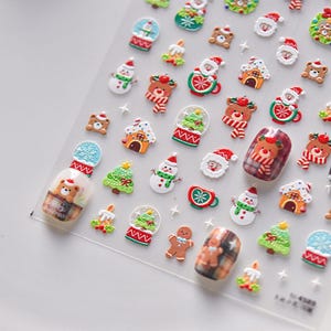 May include: A sheet of Christmas-themed nail stickers featuring a variety of designs, including snowmen, Christmas trees, gingerbread men, Santa Claus, and bears. The stickers are on a clear background and are ready to be applied to nails.