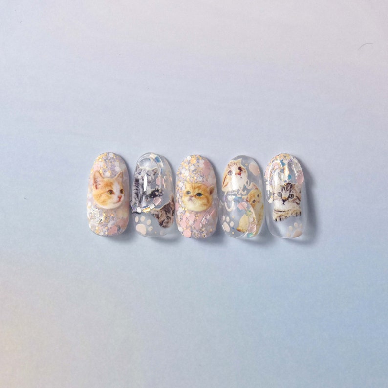 May include: Five clear nail polish bottles with glitter and cat designs. Each bottle has a different cat design.