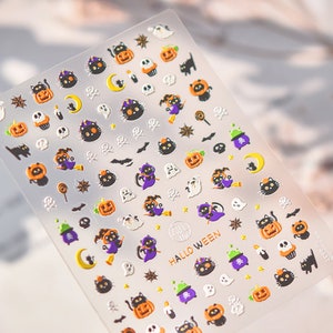 Peut inclure: Une feuille d'autocollants sur le th&egrave;me d'Halloween avec des chats noirs, des citrouilles, des fant&ocirc;mes, des &eacute;toiles, des lunes et d'autres motifs effrayants. Les autocollants sont sur un fond transparent et ont une finition brillante. Le texte "HALLOWEEN" est imprim&eacute; en or sur la feuille.