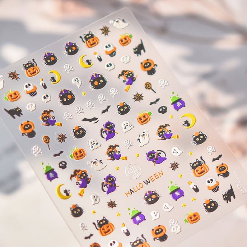 Peut inclure: Une feuille d'autocollants sur le th&egrave;me d'Halloween avec des chats noirs, des citrouilles, des fant&ocirc;mes, des &eacute;toiles, des lunes et d'autres motifs effrayants. Les autocollants sont sur un fond transparent et ont une finition brillante. Le texte "HALLOWEEN" est imprim&eacute; en or sur la feuille.