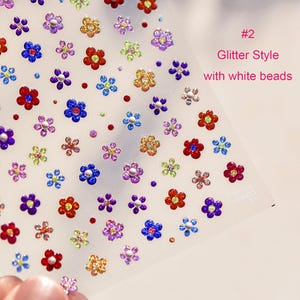 May include: A sheet of colorful flower stickers with glitter and white beads. The stickers are on a clear background and are arranged in a random pattern. The text "#2 Glitter Style with white beads" is in the upper right corner of the sheet.