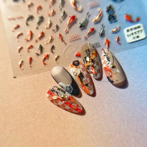 May include: Five artificial nails with a Japanese theme, featuring koi carp, floral designs, and checkered patterns in orange, red, black, and beige. A sheet of koi fish stickers is visible in the background.