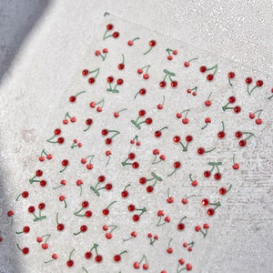 May include: A sheet of clear adhesive stickers with red and green cherry designs. The cherries have a shiny, almost gem-like appearance.