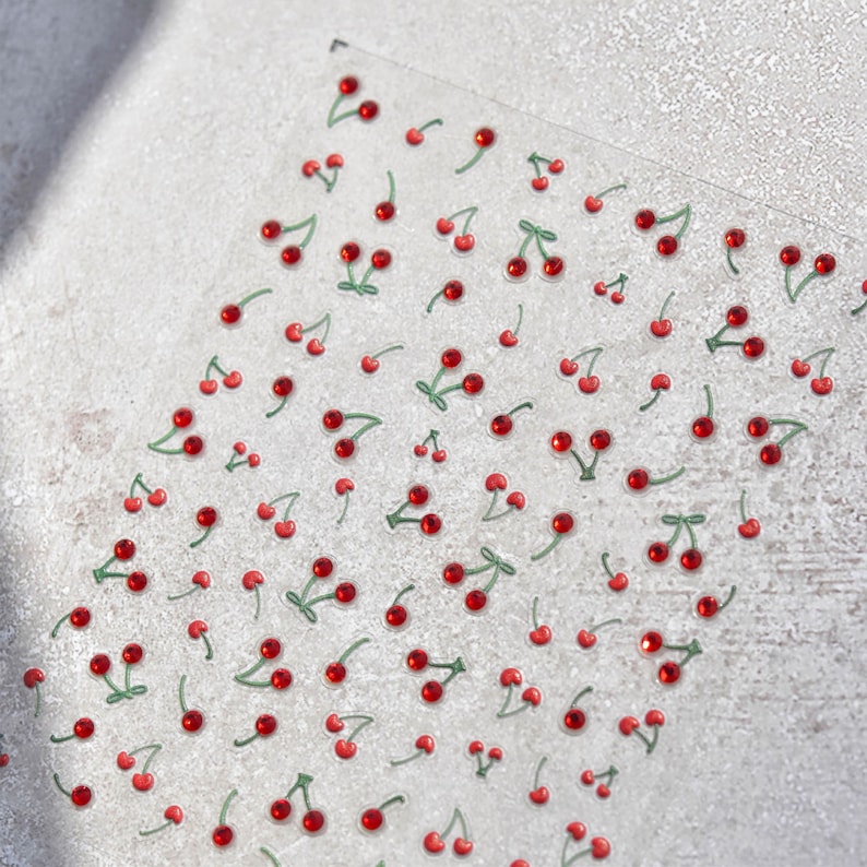 May include: A sheet of clear adhesive stickers with red and green cherry designs. The cherries have a shiny, almost gem-like appearance.