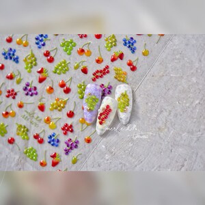 Pu&ograve; includere: Un foglio di adesivi per l'arte delle unghie con immagini di uva, fragole e ciliegie. Gli adesivi sono su uno sfondo bianco. Il testo "merle_x_lemon" &egrave; visibile nell'angolo in basso a destra dell'immagine.
