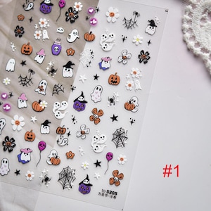 May include: Clear sheet of Halloween-themed nail art stickers. Designs include orange pumpkins, white ghosts, black spiders, purple witch hats, and white flowers. The sheet is labeled with the number "#1".