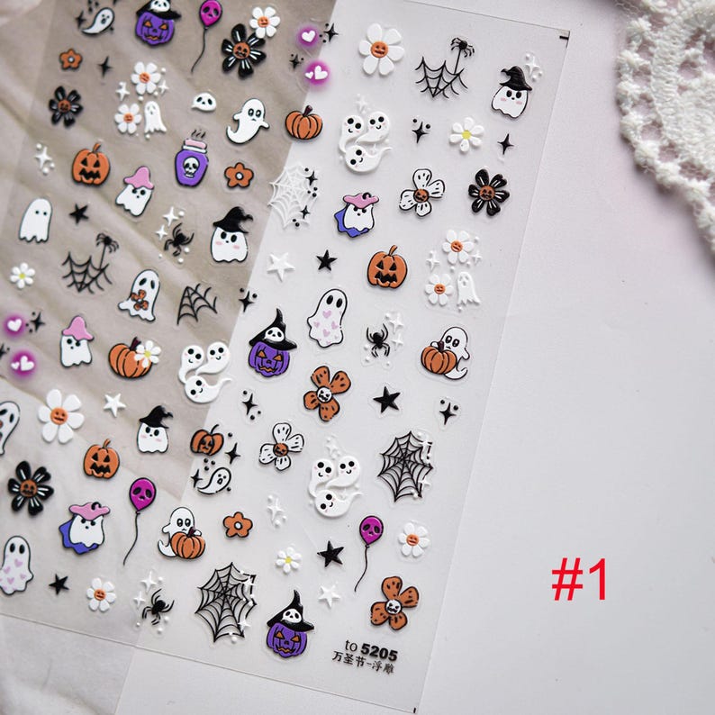 May include: Clear sheet of Halloween-themed nail art stickers. Designs include orange pumpkins, white ghosts, black spiders, purple witch hats, and white flowers. The sheet is labeled with the number "#1".