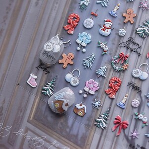 May include: A sheet of Christmas-themed nail stickers with various designs, including a gingerbread man, a snowman, a wreath, mittens, and a house. The stickers also feature the words "Happy" and "Merry Christmas".