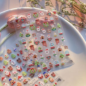 May include: A sheet of clear plastic with a variety of Christmas-themed stickers. The stickers feature images of Santa Claus, snowmen, reindeer, Christmas trees, gingerbread men, and snow globes. The stickers are perfect for adding a festive touch to gifts, cards, or crafts.