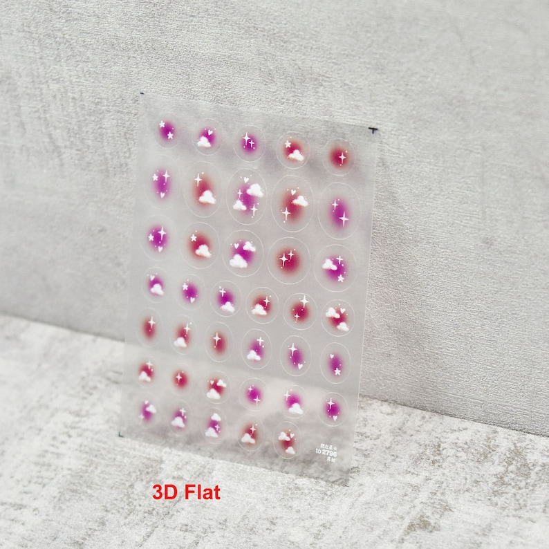 May include: A sheet of clear nail stickers with a variety of pink, white, and red cloud and star designs. The stickers are arranged in a grid pattern on the sheet. The sheet is labeled "3D Flat".