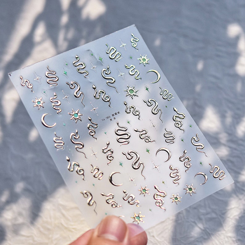 May include: A sheet of clear sticker paper with silver snake, crescent moon, and star designs. The stickers are arranged in a repeating pattern. The text "La 365" is printed on the sheet.